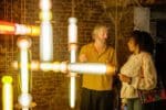 A complex suspended lighting structure with two people talking in the background. Curiousa Lighting Design at Light. Image Sam Frost.