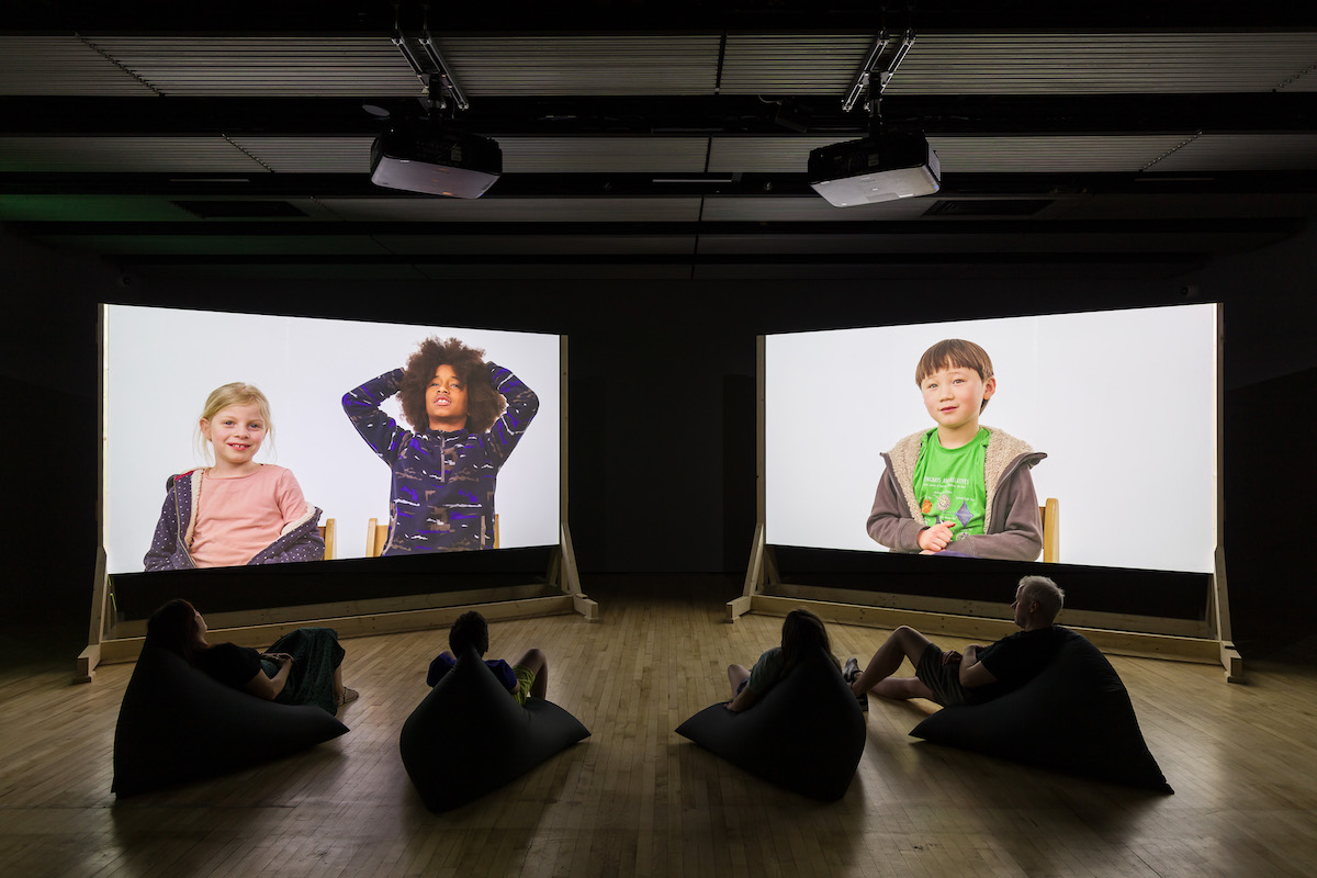 Two projector screens displaying films of children talking about the future. Installation view of Cornelia Parker, Dear Earth: Art and Hope in a Time of Crisis. Photo: Mark Blower. Courtesy the Hayward Gallery.