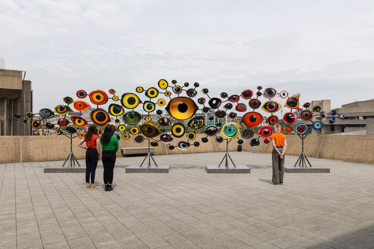 Three people looking at a large artwork on the roof of the Hayward Gallery. Installation view of Jenny Kendler, Dear Earth: Art and Hope in a Time of Crisis. Photo: Mark Blower. Courtesy the Hayward Gallery.