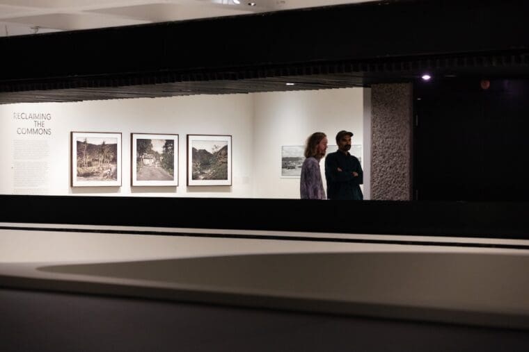 a view across the upper floor of the gallery space at two people talking