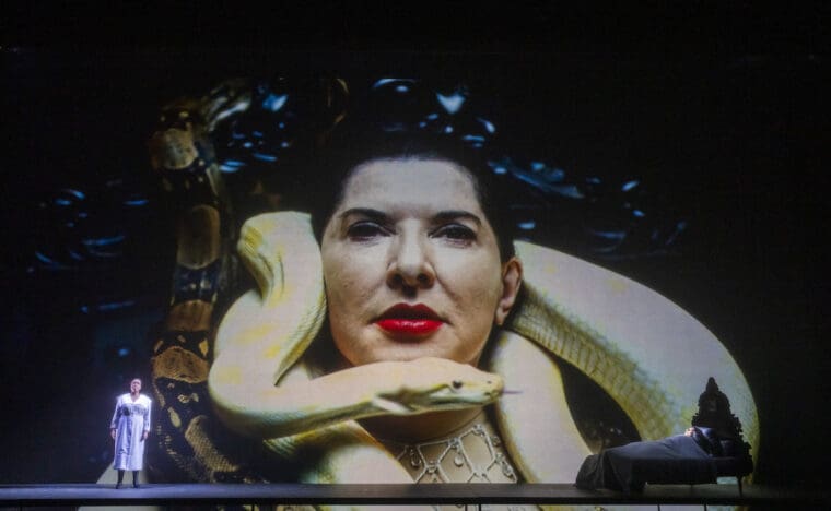 Nadine Benjamin (Desdemona) and Marina Abramović (Maria Callas, on screen and in bed) in 7 Deaths Of Maria Callas an Opera Project by Marina Abramović with music by Marko Nikodijević @ London Coliseum. Conducted by Yoel Gamzou. Marina Abramović, Director, actor, set designer and scenography (Maria Callas). (Opening Night 03-11-2023) ©Tristram Kenton 10-23 (3 Raveley Street, LONDON NW5 2HX TEL 0207 267 5550 Mob 07973 617 355)email: tristram@tristramkenton.com