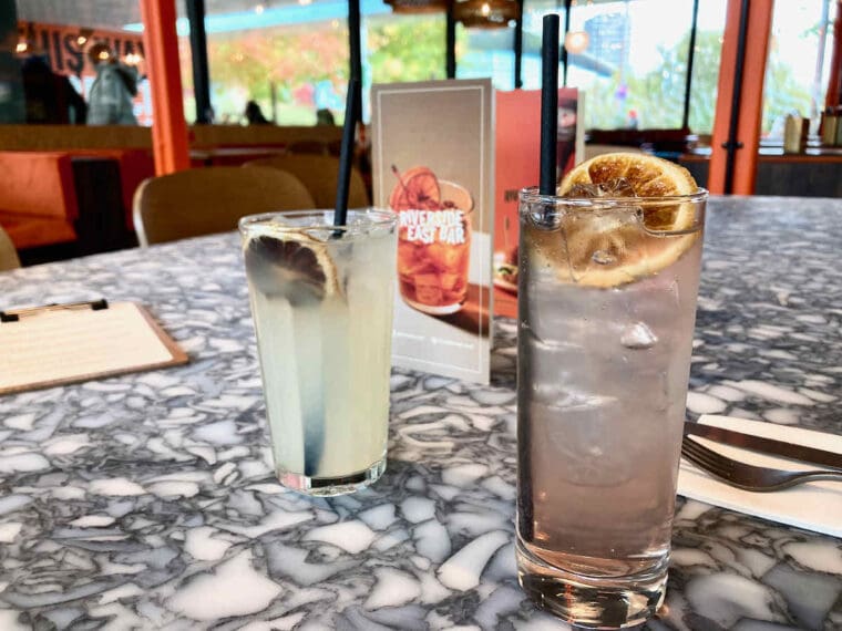 Two drinks served in tall Collins glasses with slices of blood orange and black straws; on the left lemonade and on the right a rosé vermouth cocktail.