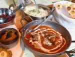 Jugad restaurant's Delhi butter chicken curry with red tomato sauce and swirls of non-dairy cream with rice and naan bread in background.