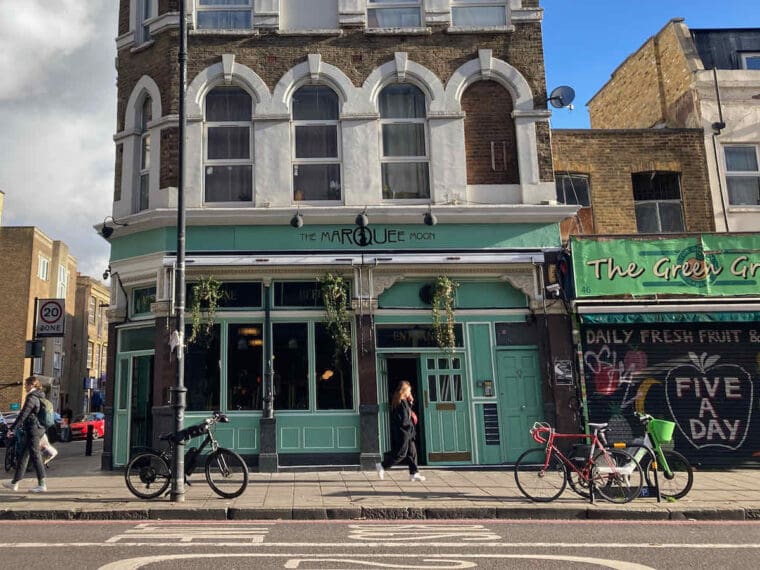 Daytime exterior of The Marquee Moon pub with green paintwork and tumbling plants on Stoke Newington Road with three bikes parked outside.