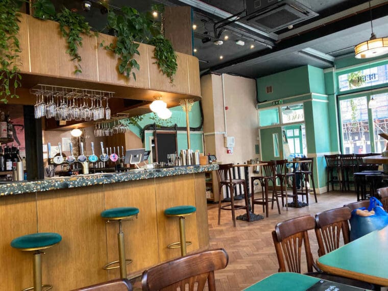Interior shot of The Marquee Moon pub in Dalston, wood panelling and velvet stools around the bar, parquet floor and green walls.
