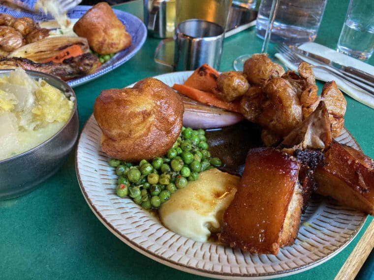 Sunday roast dinner of braised pork belly, parsnip puree, peas, Yorkshire pudding, carrots and roast baby potatoes.