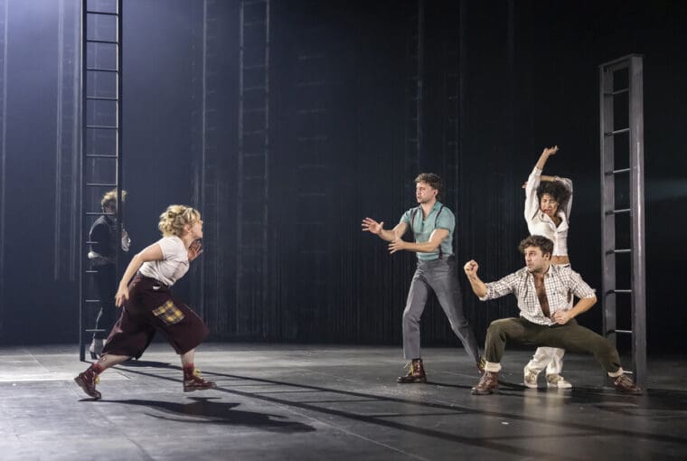 RSC A Midsummer Nights Dream Barbican pic credit Armani Ur-Rub; left to right shows Hermia, Lysander, Demetrius and Helena on a dark stage amidst several vertical ladders.