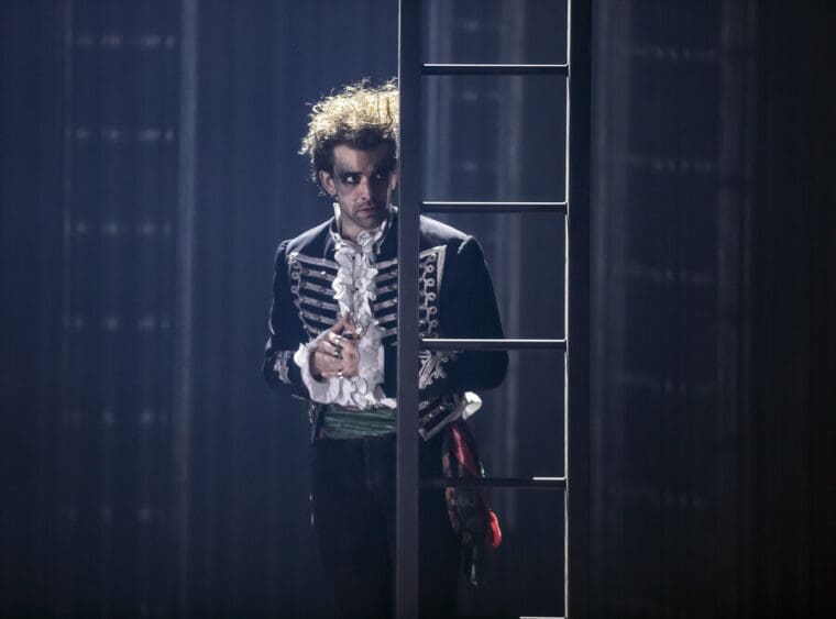 RSC A Midsummer Nights Dream Barbican pic credit Armani Ur-Rub; Oberon played by Andrew Richardson dressed in braided Hussar's jacket at a ladder on a dark stage.