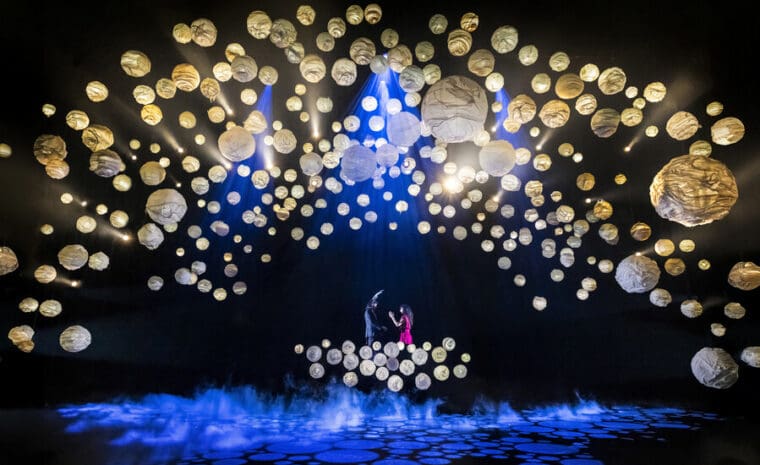 RSC A Midsummer Night's Dream Barbican pic credit Armani Ur-Rub; a dark stage lit with scores of paper globes as Titania and Bottom fall in love on a raised platform.