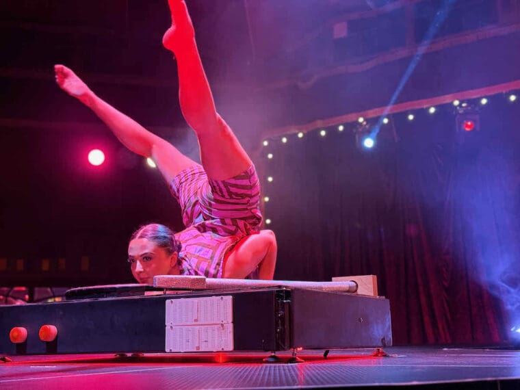 A contortionist lying on her front, on a giant record turntable, with her legs behind her, high up in the air performs at The Ruckus by The Revel Puck Circus.