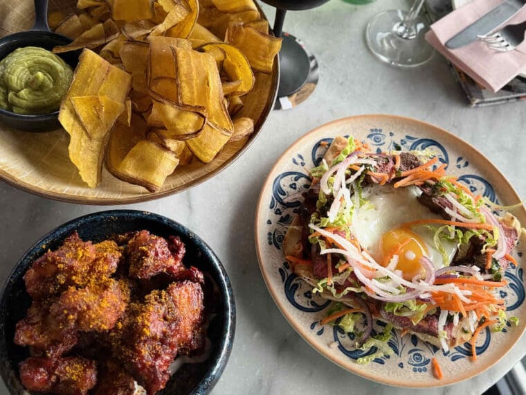 Shot from above of plantain chips, guacaomole, spice coated cauliflower wings and Asian beef flatbread with an egg served at Savage Garden rooftop bar, Tower Hill, London.