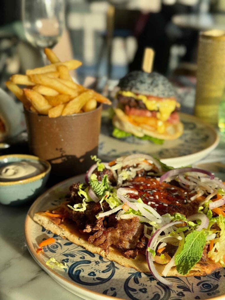 Pulled Funky Mushroom main course served on flatbread with vegetable slaw, shown with chips and burger in background at Savage Garden rooftop bar, Tower Hill, London.