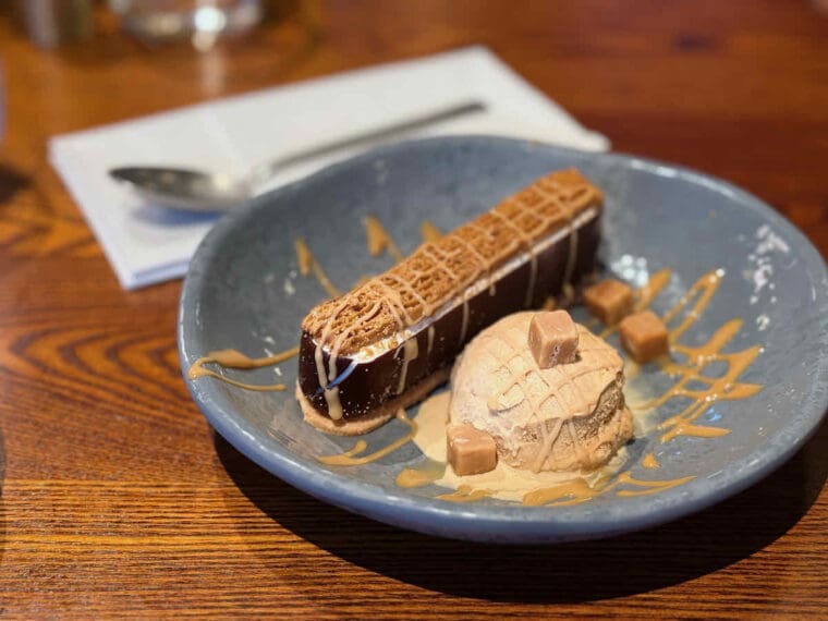 Toffee cheesecake with caramel ice cream and caramel chunks served in a grey bowl at Waterfront Street Kitchen and Bar at Royal Victoria Dock.