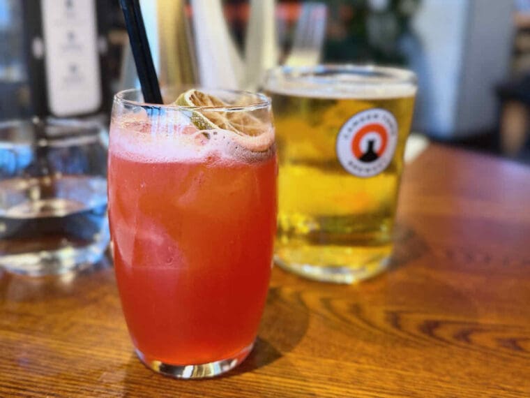 Bright red rum cocktail with lime slice at Waterfront Street Kitchen and Bar at Royal Victoria Dock. A pint of lager in the background.