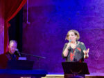 Christine Bovill on stage performing Piaf Revisited at Wilton's Music Hall, East London. Pianist Michael Roulston is to the left.