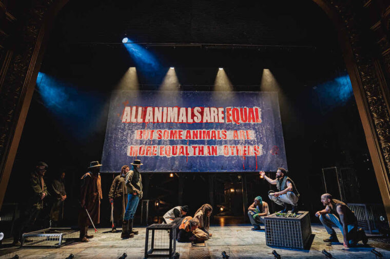 Napoleon bargains with farmers in Animal Farm at Stratford East; the backdrop displays the words