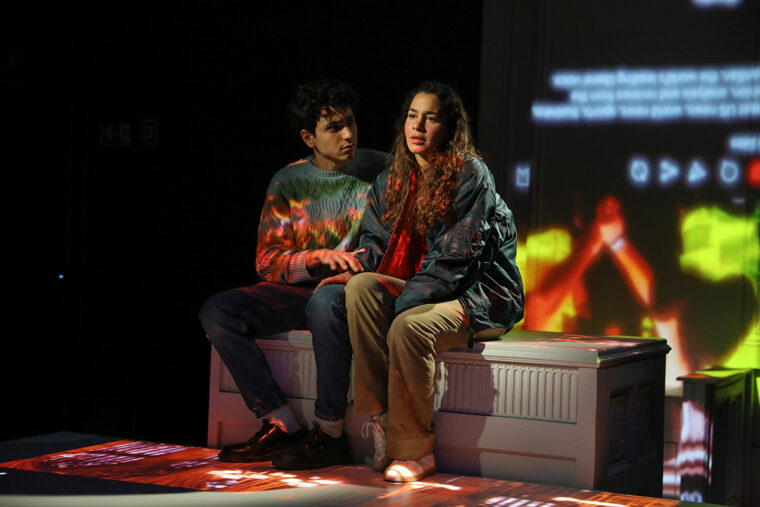 Antigone [on strike] at Finsbury Park Theatre, photos by Nir Segal, Ali Hadji-Heshmati as Eammon sits by Hiba Medina as Antiya.