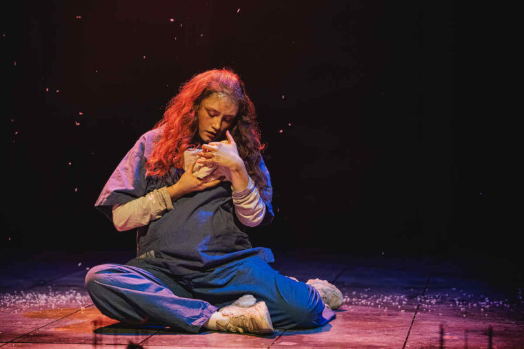 Brydie Service at Clara the chicken in Animal Farm at Stratford East; a pregnant woman with long red hair, seated on the floor, cradles tiny young close to her face. Photo credit Kirsten McTernan