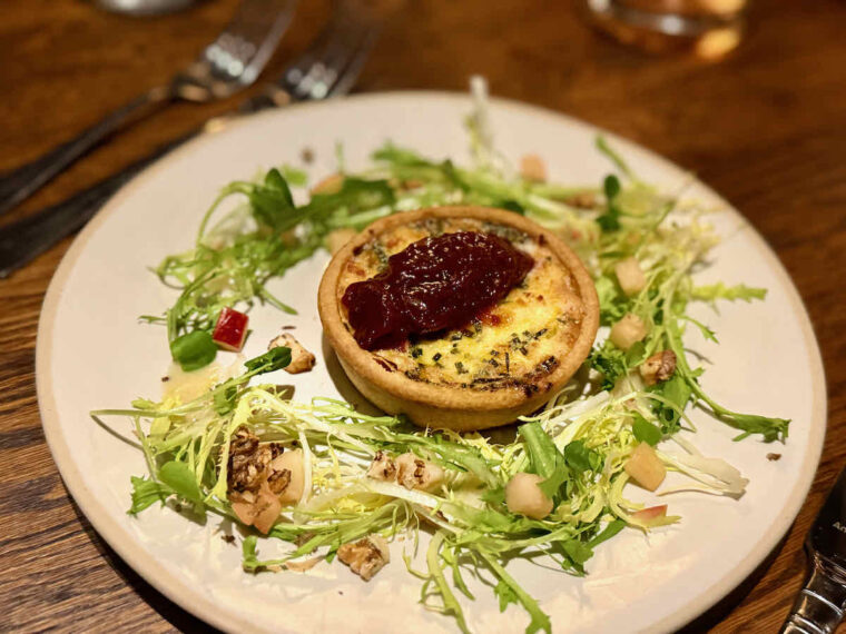 Starter dish of leek and goat's cheese tart with blob of caramelised onion, surrounded by frisée lettuce, apple and walnut. As served at The Royal Forest, Epping Forest, Heartwood Inns.