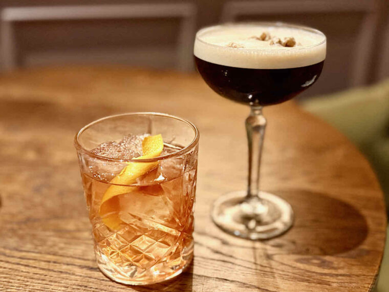 Cocktails served after dinner at The Royal Forest, Epping Forest, Heartwood Inns; left an Old Fashioned in tumbler with orange zest, right an Espresso Martini in a coupe glass. On a wooden table. 