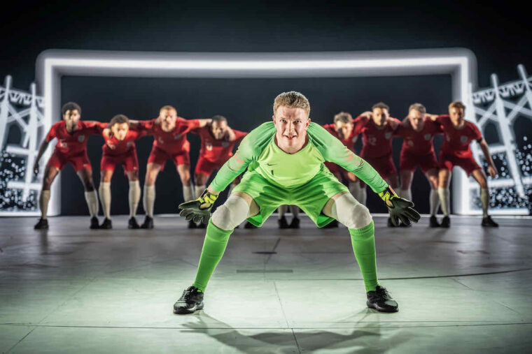 NT Dear England, Josh Barrow as goalkeeper Jordan Pickford crouching in goal with other players behind him. Photo by Marc Brenner.