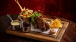 A wooden platter of prepared grouse, liver pate on toast, a side of greens and bacon, jus and bread sauce.