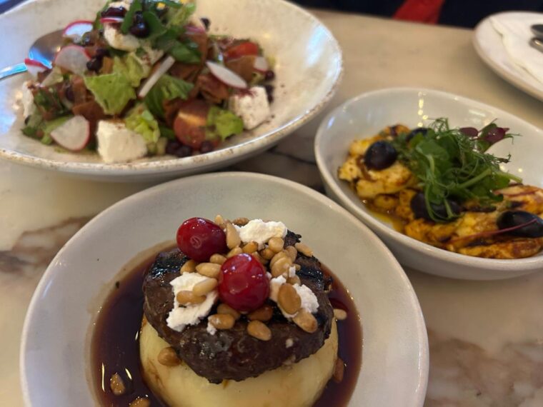 A plate of kofta with cherries at Villa Mamas restaurant with plates of salad and halloumi cheese in the background
