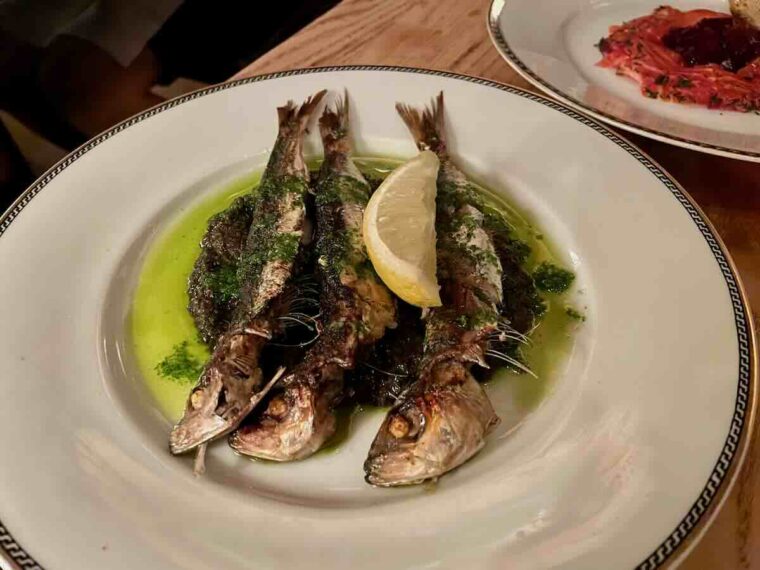 Grilled sardines with green tapenade and a lemon slice on top.