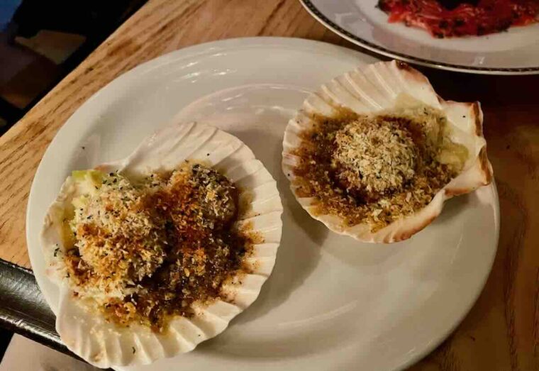 Scallops in their shells with grated cheese and breadcrumbs.
