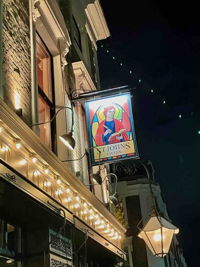 St John's Tavern exterior showing the sign hanging outside with a portrait of St John in front of stained glass.