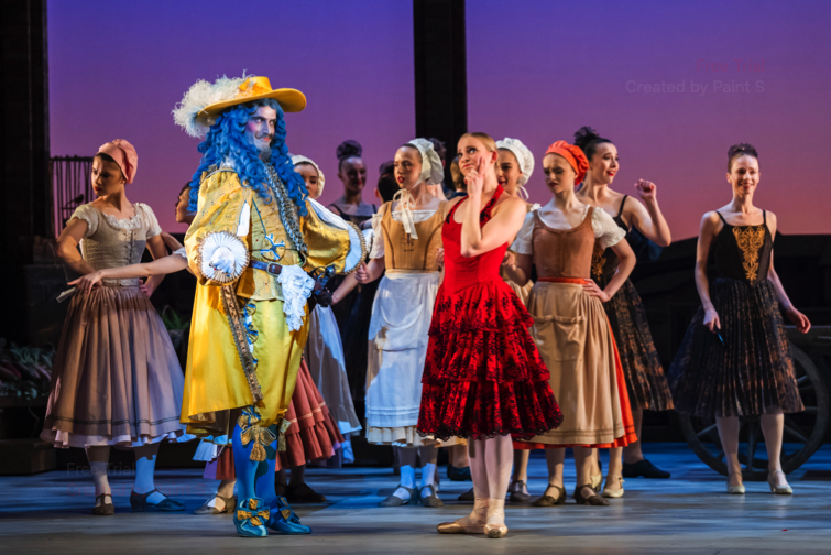 An extravagantly apparelled Gamache, wearing a long blue wig and feathered hat tries to impress Kitri
