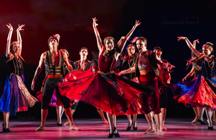 A gypsy woman in a full red skirt performs a boisterous dance egged on by other gypsies
