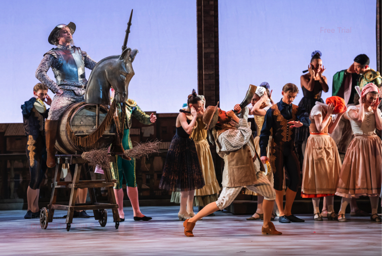 Don Quixote riding a makeshift horse on wheels arrives in the village preceded by his servant Sancho Panza