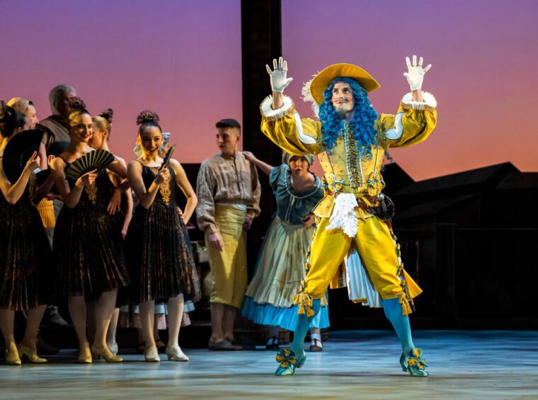 The fop Gamache, richly apparelled in bright yellow, wth plumed hat, white gloves and long blue wig.