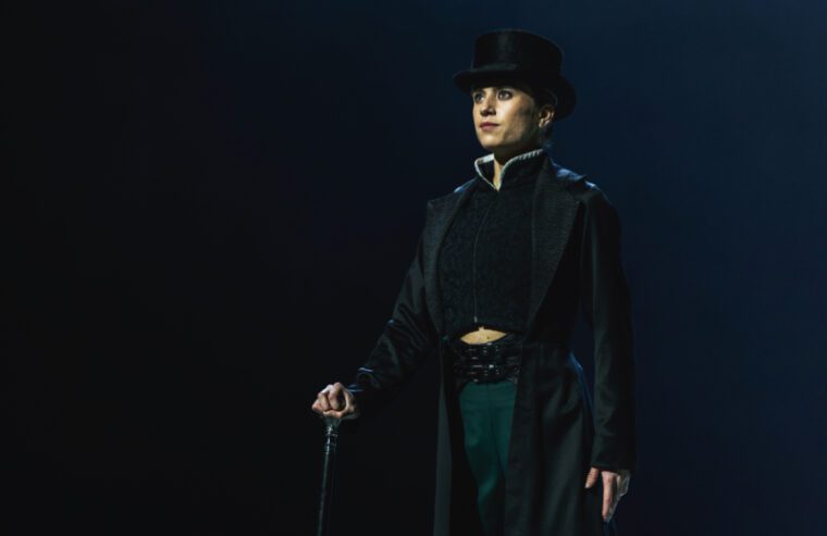 Gentleman Jack: a dancer in top hat, frock coat and green trousers, stands holding the silver top of her cane
