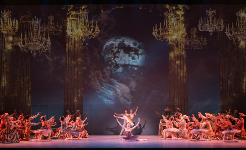 The finale of ENB The Sleeping Beauty: in a hall with hanging candelabra the whole court kneels either side of the stage in honour of the Prince and Princess, who pose at the back ,and the Lilac Fairy, who sit on the stage in front of them