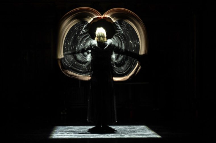 Against a black background, a woman with her back to us creates optical illusions with her moving arms