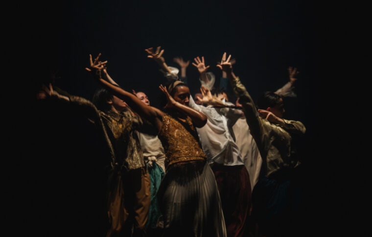 Shechter: In The Brain A cluster of dancers raise their arms with splayed fingers up to heaven