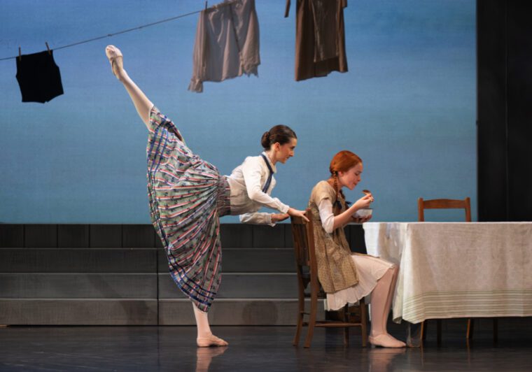 Anne of Green Gables: Anne sits at the table eating from a bowl. Behind her, a woman in a white blouse and printed pleated skirt leans on the chair with one left lifted in high arabesque, against a background of cloths drying on the line.