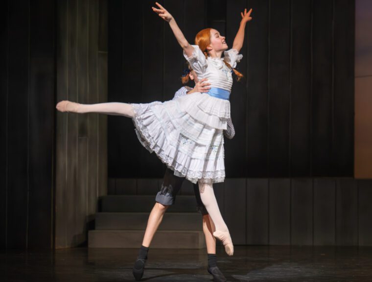 Anne of Green Gables: Anne in her brand new white, flouncy dress with blue belt, is lifted by a boy. She has her right leg lifted in arabesque, arms raised and a happy smile.