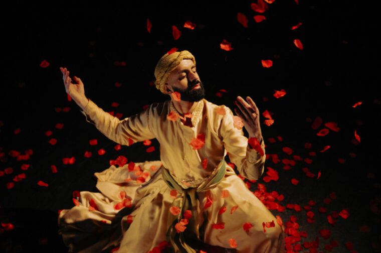 Songs of the Bulbul: the dancer, wearing a white turban and dervish robe, sits under a shower of rose petals.