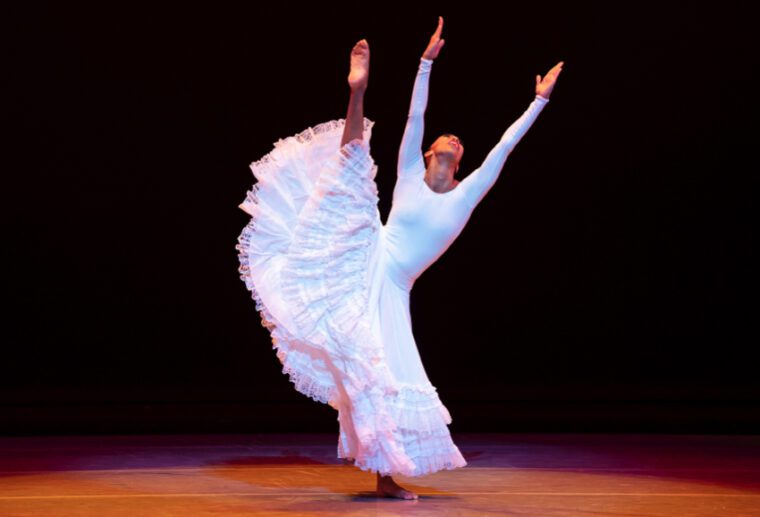 Alvin Ailey American Dance Theater: a woman in a long, ample, flouncy skirt raises her right leg up above her head, arms and head raise to heavan