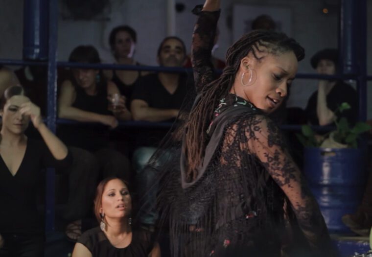 Dance Umbrella 26 An African woman wearing a black lace shawl dances flamenco wached by a group of women