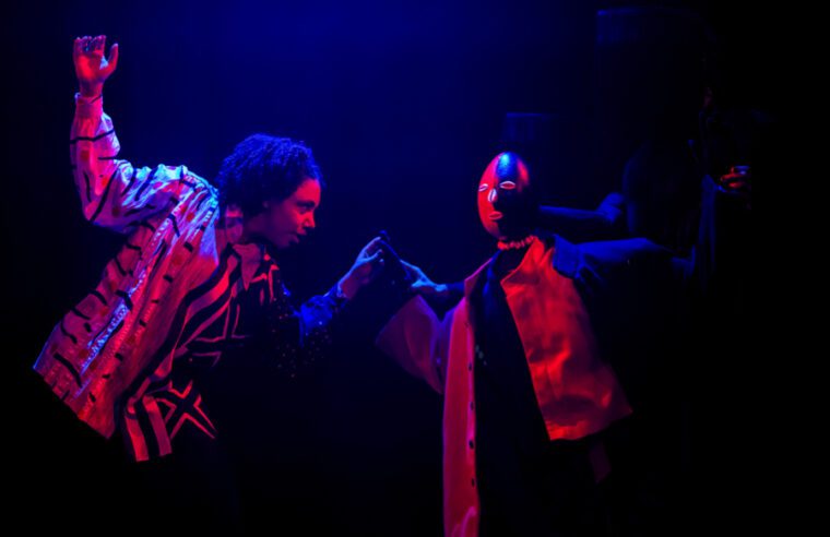 Eshu at the Crossroads - under blue light, the traveller engages ina dance with the Eshu puppet who sports his black and red colours
