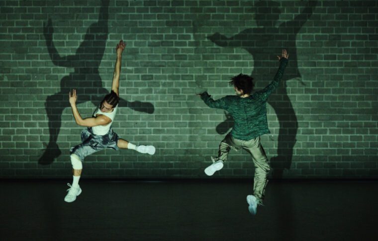 Hang Time: under a greenish light, two men jump up, casting shadows on a brick wall