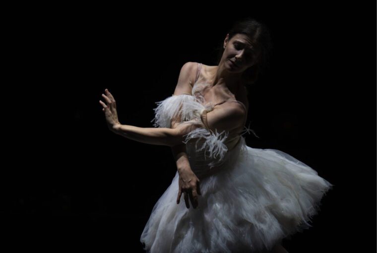 Firebird - A Double Bill A woman in a white swan tutu poses with arms crossed in front of her vody, head leaning over her left shoulder