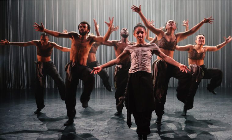 Tellus - exuberant ensemble dancing, with arms stretched out wide, stomping with alternate legs