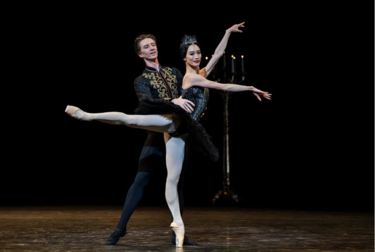 A Centenary Celebration: in the Black Swan pas de deux the man stands behind the ballerina holding her waist as she stands in 90 degree arabesque, arms stretched forward.